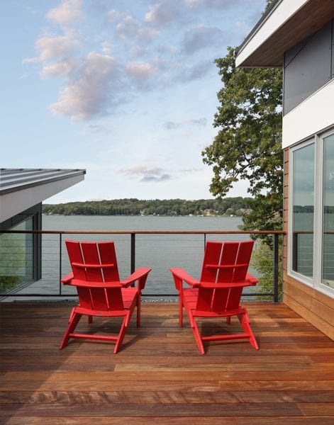 picture of a deck with two red chairs facing the lake