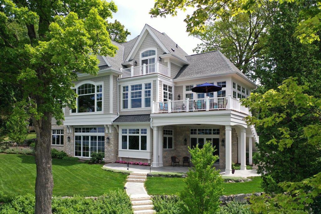 gray and stone home with a balcony and patio - Cedar Lane | A Colby Construction Traditional Lake Home